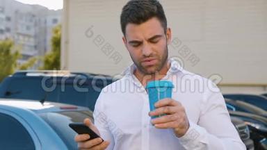 <strong>办公大楼</strong>附近的停车场上有一个英俊的男人，使用智能手机和饮用美味的咖啡。 看上去很满意